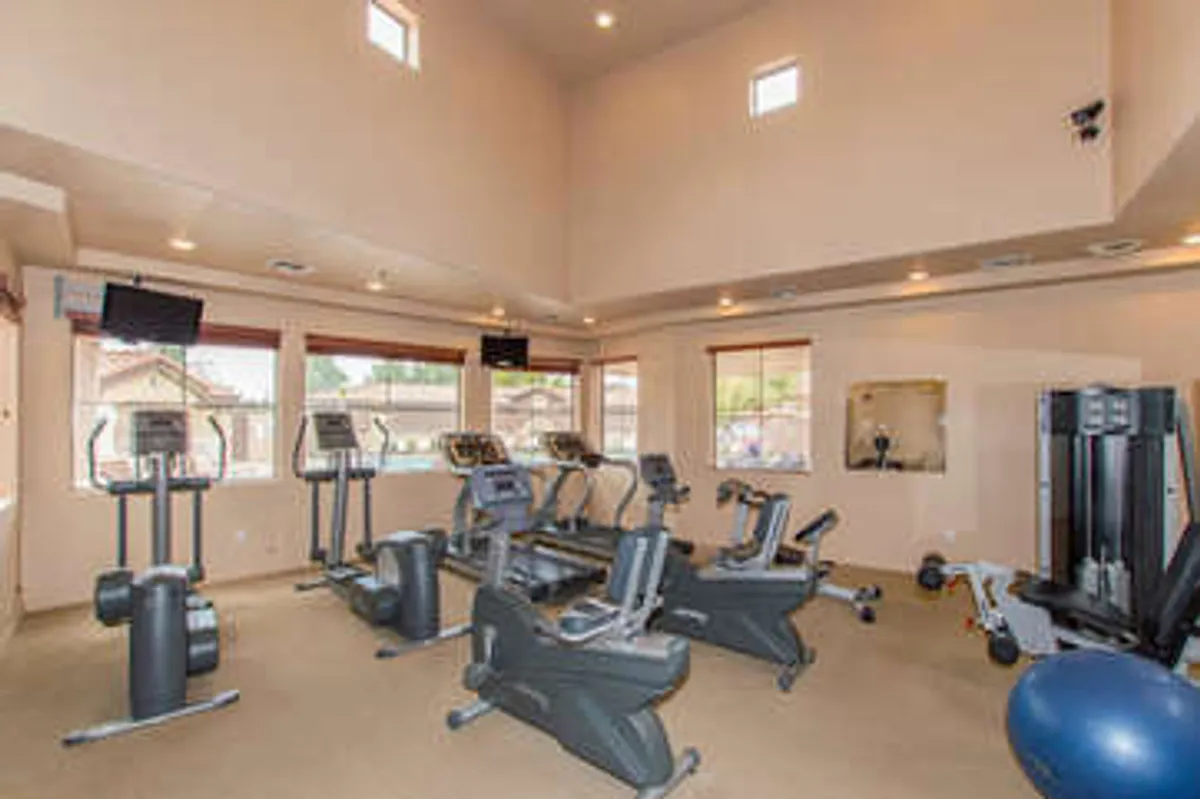 A modern, well-equipped fitness center featuring a range of exercise equipment, large bright windows, and multiple televisions. The gym appears spacious, clean, and motivational, ideal for both serious workouts and casual exercise.