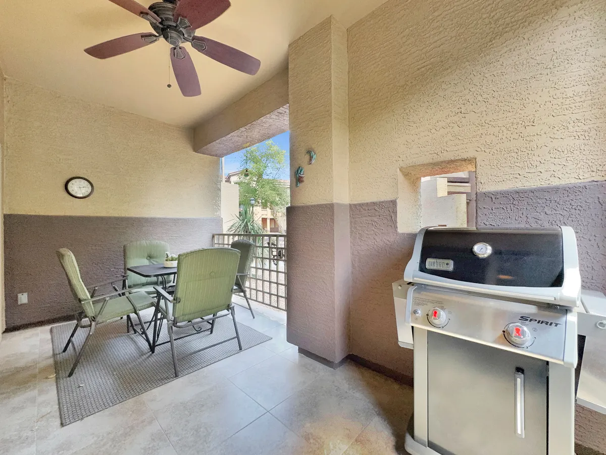 This image presents a patio with a dining table and chairs, grill, ceiling fan, and wall art, creating a versatile space for outdoor dining, barbecuing, and relaxing. The design invites both casual brunches and sunset dinners, with ample seating for gatherings.