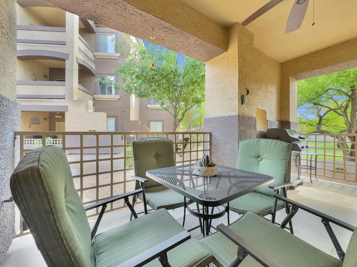 This image features a private outdoor seating area with a table topped by a decorative plant, set against a backdrop of lush greenery visible beyond the railing. The setup is ideal for enjoying morning coffee, afternoon relaxation, or entertaining guests, and the sunlight filtering in gives the space a serene, inviting atmosphere.